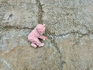 A baby in a fuzzy pink bear outfit on the pavement