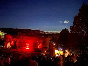Red tinted stage lights and crowd at Red Rocks Amphitheatre above Denver in the distance
