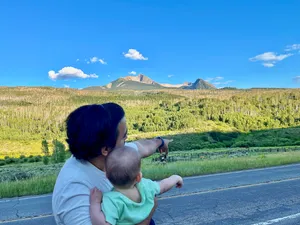Andrew holding a baby on a rural highway, pointing to a distant horse paddock