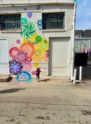 A toddler running in front of rainbow colored graffiti art on white brick