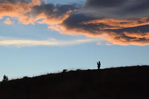 Silhouette on a hill beneath blue sky and orange clouds at sunset