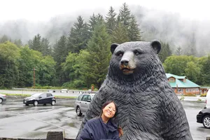 Woman and standing bear statue in front of mist and trees