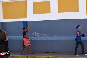 Woman with a bucket on her head in front of a blue and yellow wall