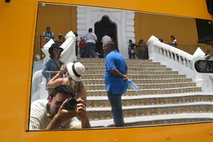 A reflection from a mirror on the side of a school bus including the photographer and the steps to acolonial building