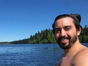 Bearded shirtless man on a lake with trees on the shore