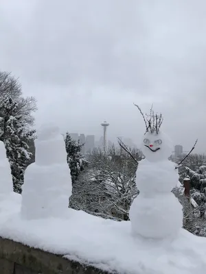 Small snowman with a devious grin in the foreground above the Space Needle on a gray day