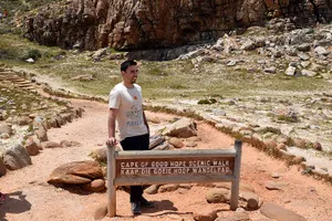 Man leaning on a sign that says CAPE OF GOOD HOPE SCENIC WALK
