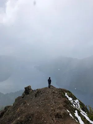 Person standing on mountaintop over alpine lake in fog and snow