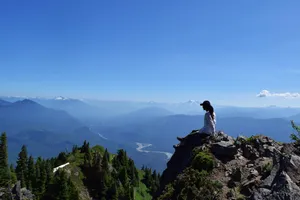 Woman on mountain promontory overlooking valley, stream, and mountain layers