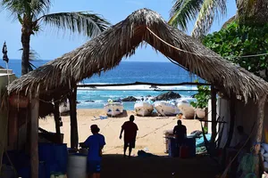 People in shadow under a thatched roof and boats ashore by the ocean