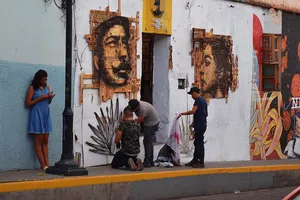 Muralists at work and a woman in a blue dress leaning against the wall